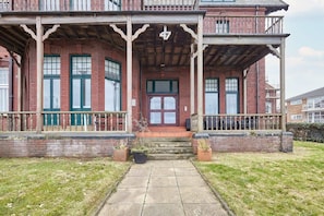 Een tweelaags bakstenen huis met een veranda, een voordeur en een kleine tuin met potplanten.