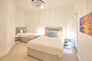 A hotel room with a large bed, a smaller bed, a chandelier, and a painting on the wall.