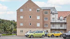 Un edificio residencial de varios pisos con fachada de ladrillo, múltiples ventanas y un estacionamiento con varios automóviles.