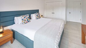 Un dormitorio con una cama grande, una mesita de noche de madera, una lámpara de noche y una puerta blanca.