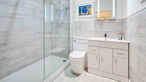 Un baño moderno con ducha de mampara de vidrio, inodoro blanco y tocador con almacenamiento.