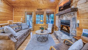 Interior acogedor de una cabaña con chimenea de piedra, paredes de madera y un sofá con cojines estampados.