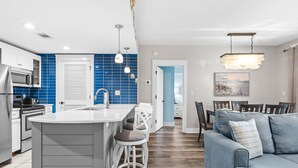 A modern kitchen with a central island, white bar stools, and a blue tiled backsplash. - Rates Reduced! Oversized Balcony, Lagoon Pool Views! Hot Tub, Beach Tram, Gym (Miramar Beach)