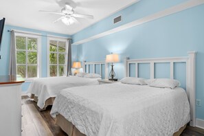 Une chambre avec deux lits, un ventilateur de plafond et une fenêtre avec des rideaux.