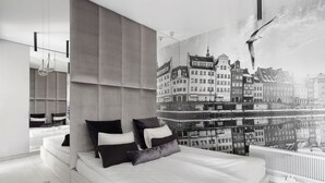 Een moderne slaapkamer met een groot bed, een stadsgezicht muurschildering op de wand en een uitzicht op gebouwen door het raam.