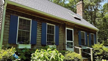 A two-story house with a gabled roof, a brick chimney, and a front porch with steps.
