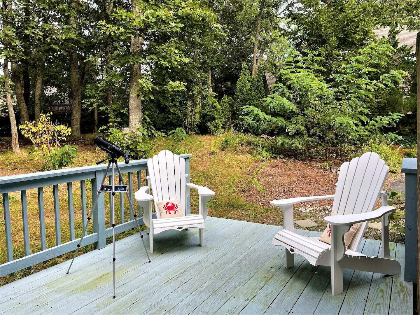 A wooden deck with two white Adirondack chairs and a telescope.