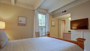 Ett hotellrum med en stor säng, en platt-TV som är monterad på väggen, ett fönster med gardiner och en inramad tavla på väggen.
