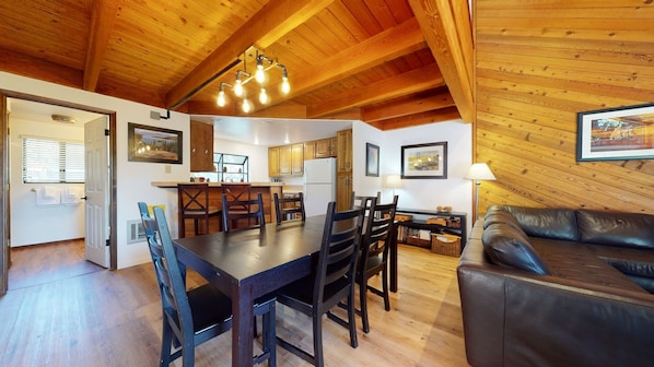 A cozy interior with a wooden ceiling, a dining area with a table and chairs, a kitchen with wooden cabinets, and a leather sofa.