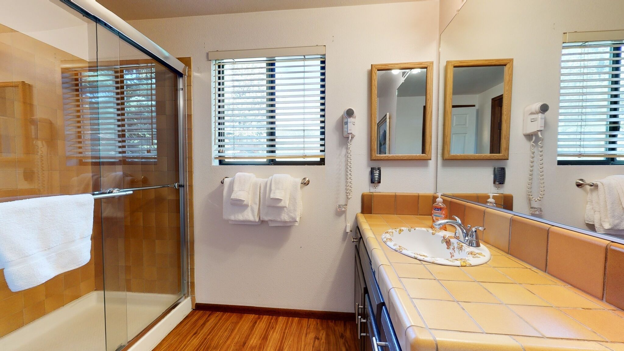 A bathroom with a glass shower enclosure, a sink with a floral basin, and two mirrors.