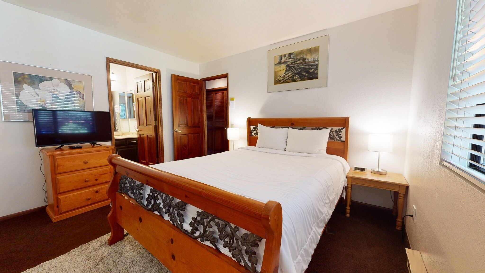 A bedroom with a wooden bed, a TV on a dresser, and a painting on the wall.