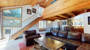 Un vaste espace de vie agrémenté d’un escalier en bois, de canapés en cuir et d’un coin repas.