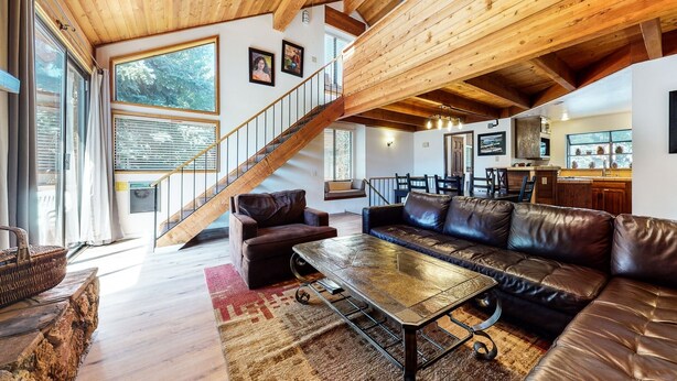 Un vaste espace de vie agrémenté d’un escalier en bois, de canapés en cuir et d’un coin repas avec une cuisine en arrière-plan.