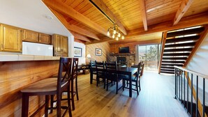 Un intérieur en bois comprenant un coin repas, une cuisine et un escalier menant à un balcon.