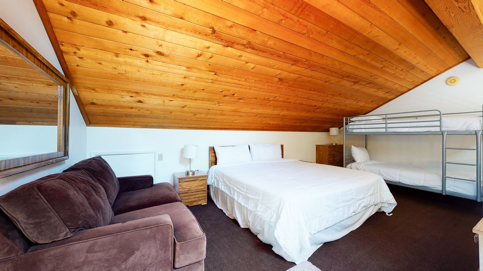 A room with a wooden ceiling, bunk beds, a sofa, and a bedside table.