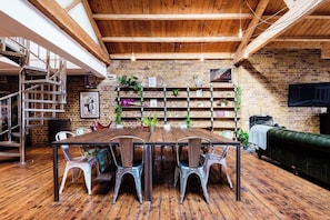 A rustic dining area with a wooden table and metal chairs, surrounded by brick walls and shelves with plants.