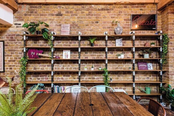 Una pared de ladrillo rústica con estanterías metálicas, algunas con libros y adornos, y una mesa de madera al frente.
