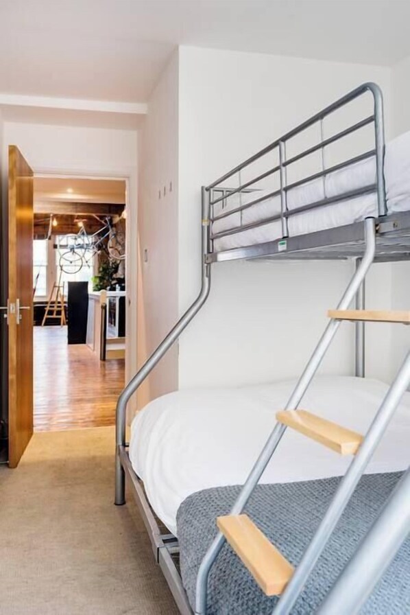 A bunk bed with metal railings and wooden steps, a carpeted floor, and a doorway leading to a room with a bicycle and a ladder. - East London loft penthouse with epic roof terrace and loads of space (London)