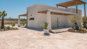 Ein modernes, zweistöckiges Haus mit flachem Dach, einer überdachten Terrasse und einer Wüstenlandschaft im Hintergrund.