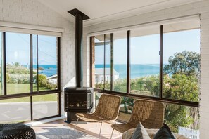 A room with a large window, a wood-burning stove, and wicker chairs.