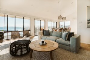 A spacious living room with a large window, a sofa, a coffee table, and a dining area with chairs.