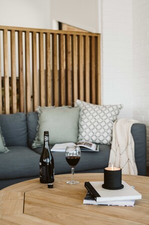 A wooden table with a bottle, a glass of red wine, a candle, and a book.
