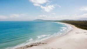 A wide sandy beach with clear blue waters and a distant mountain range. - The G At Gerroa (Gerroa)