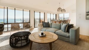 A spacious living room with a large window overlooking the sea, a grey sofa, a round wooden coffee table, and wicker chairs. - The G At Gerroa (Gerroa)
