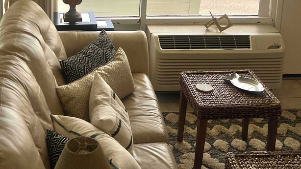 A living room with a large window overlooking a beach, a sofa, a table, and a chandelier. - Ocean Breeze - Ocean Front at Symphony Beach Club! (Ormond Beach)
