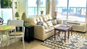 A living room with a sofa, a coffee table, a TV, a lamp, and a view of the outdoors. - Ocean Breeze - Ocean Front at Symphony Beach Club! (Ormond Beach)