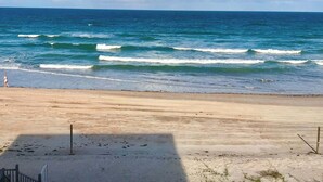 A beach with waves, a clear sky, and a person in the distance. - Ocean Breeze - Ocean Front at Symphony Beach Club! (Ormond Beach)
