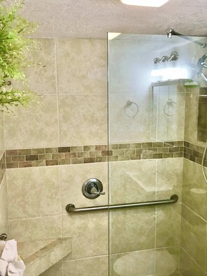 A glass-enclosed shower with a handrail, a tiled wall with a mosaic border, and a visible towel rack.