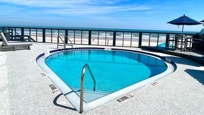 A pool with a 4 FT depth marker, a lifeguard stand, and a view of the beach. - Ocean Breeze - Ocean Front at Symphony Beach Club! (Ormond Beach)