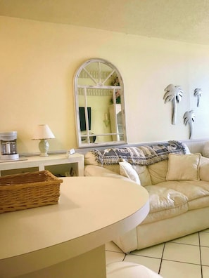A living room with a white sofa, a coffee machine, a lamp, a wicker basket, and a decorative mirror.