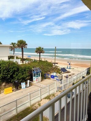 A beach view with a gated entrance, palm trees, and beach chairs. - Beach Haven -Ocean View At Symphony Beach Club (Ormond Beach)