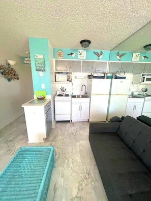 A compact living space with a kitchenette, a sofa, and a small table. - Beach Haven -Ocean View At Symphony Beach Club (Ormond Beach)