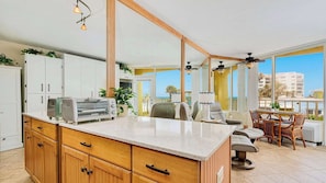 A kitchen with a large island, white cabinets, and a view of the sea. - Coastal Soul - Ocean View at Symphony Beach Club (Ormond Beach)