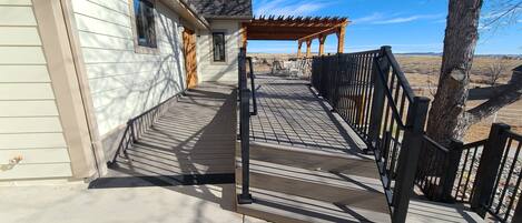 A covered outdoor area with a wooden deck, a pergola, and a black metal railing.