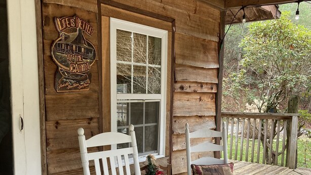 Une cabane en bois dotée d’un porche agrémenté de chaises berçantes blanches et d’une enseigne décorative.