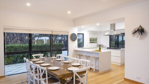 A modern kitchen with a large island, white cabinetry, and a view of the outdoors through large windows. - LUXURIOUS & INVITING TWO STOREY HOME WITH COMFORTABLY CASUAL COASTAL VIBE (Marybrook)