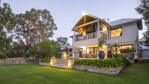 A modern two-story house with a balcony, a well-maintained lawn, and a stone wall with plants. - LUXURIOUS & INVITING TWO STOREY HOME WITH COMFORTABLY CASUAL COASTAL VIBE (Marybrook)