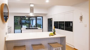 A modern kitchen with a central island, white cabinetry, and a view to the outdoors. - LUXURIOUS & INVITING TWO STOREY HOME WITH COMFORTABLY CASUAL COASTAL VIBE (Marybrook)
