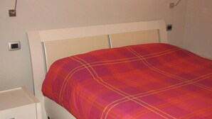 A bed with a red and orange plaid bedspread, a white headboard, and bedside lamps. - HEART OF FLORENCE APARTMENT (Firenze)