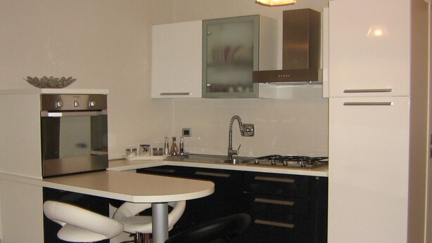 A compact kitchen with a built-in oven, a gas stove, and a sink. There is a small island with a chair and a bowl on top. - HEART OF FLORENCE APARTMENT (Firenze)