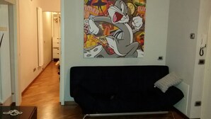 A living room with a black sofa, a white cushion, and a colorful cartoon poster on the wall. - HEART OF FLORENCE APARTMENT (Firenze)