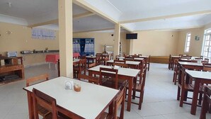 A dining area with multiple tables and chairs, a brick oven, and a television mounted on the wall. - La Vega Pousada (Guapimirim)