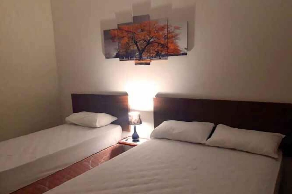 Quarto de hotel com duas camas de solteiro, mesa de cabeceira com abajur e quadro pendurado na parede.