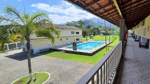 A covered balcony with a pool, a lawn, and a view of a mountain. - La Vega Pousada (Guapimirim)