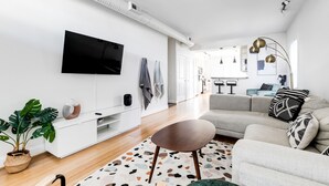 Een moderne woonkamer met een flatscreen-televisie aan de muur, een grijze bank, een salontafel en een potplant.