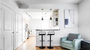 Een moderne keuken met witte kastjes, een marmeren aanrechtblad en twee zwarte barkrukken.